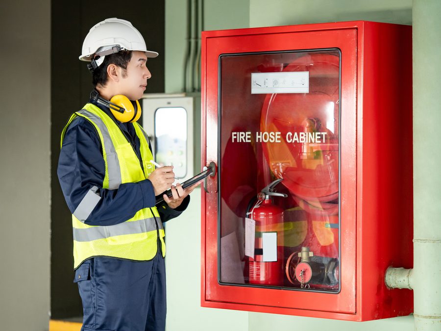 Technician with a clipboard inspecting a fire hose cabinet